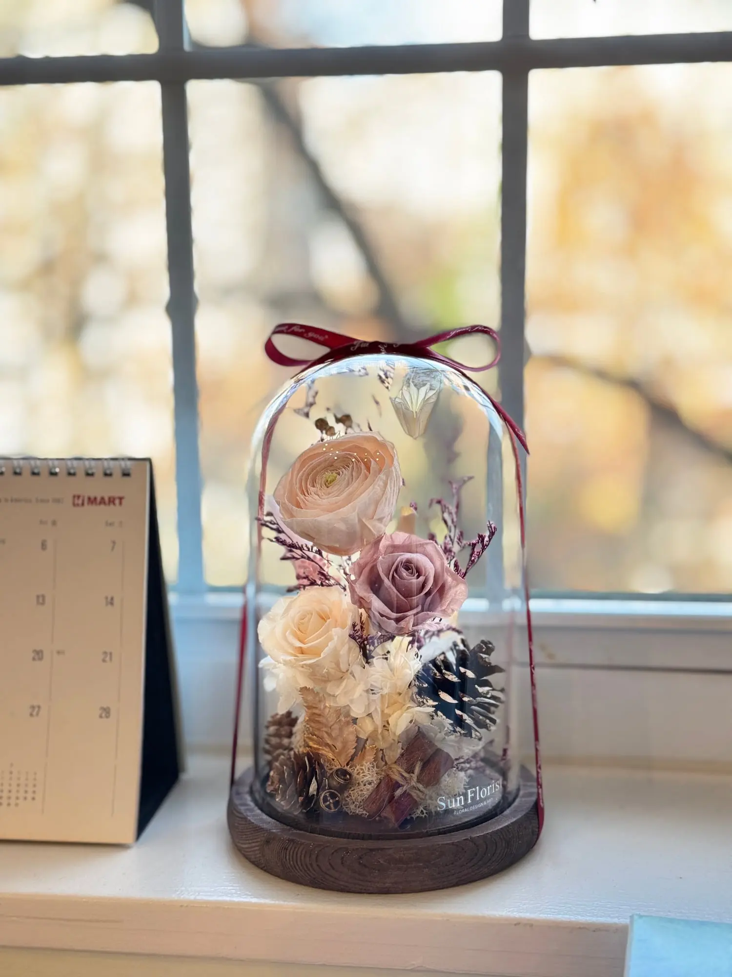Capture the warmth of fall with this enchanting preserved flower dome , featuring delicate peach and blush roses, soft hydrangeas, and natural foliage.