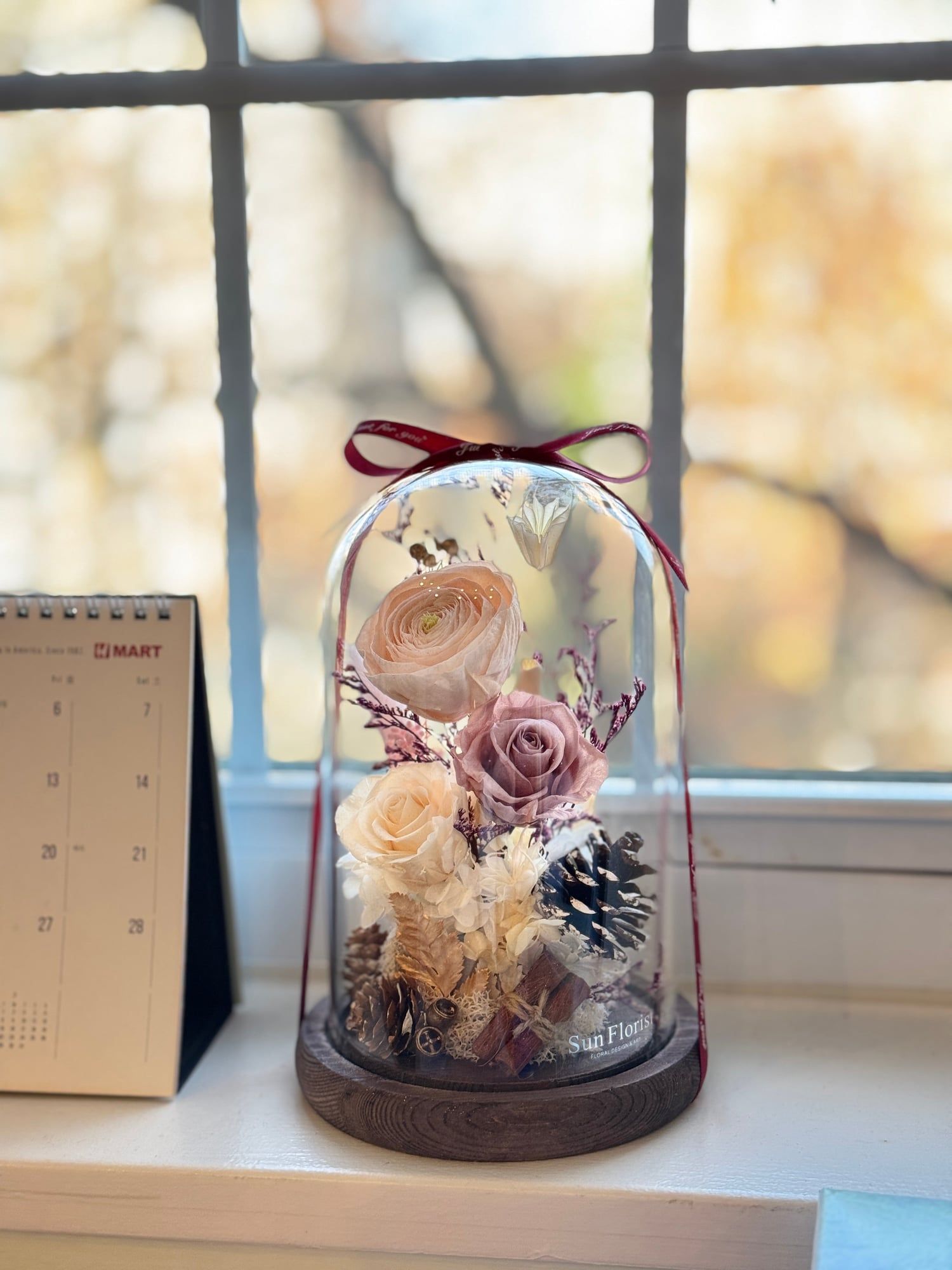 Capture the warmth of fall with this enchanting preserved flower dome , featuring delicate peach and blush roses, soft hydrangeas, and natural foliage.