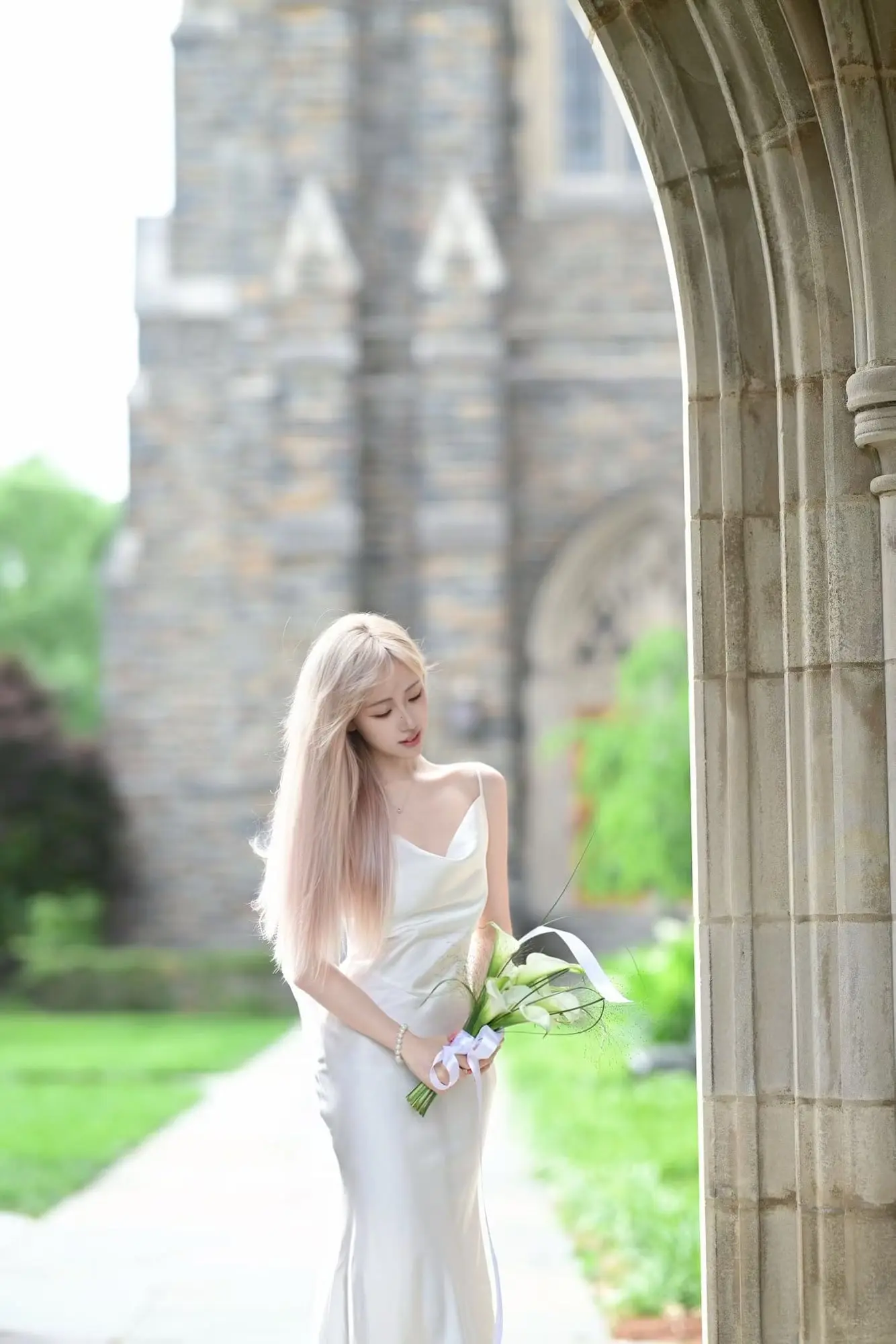 A sculptural hand-tied bouquet of white calla lilies with wild grasses and trailing satin ribbon.