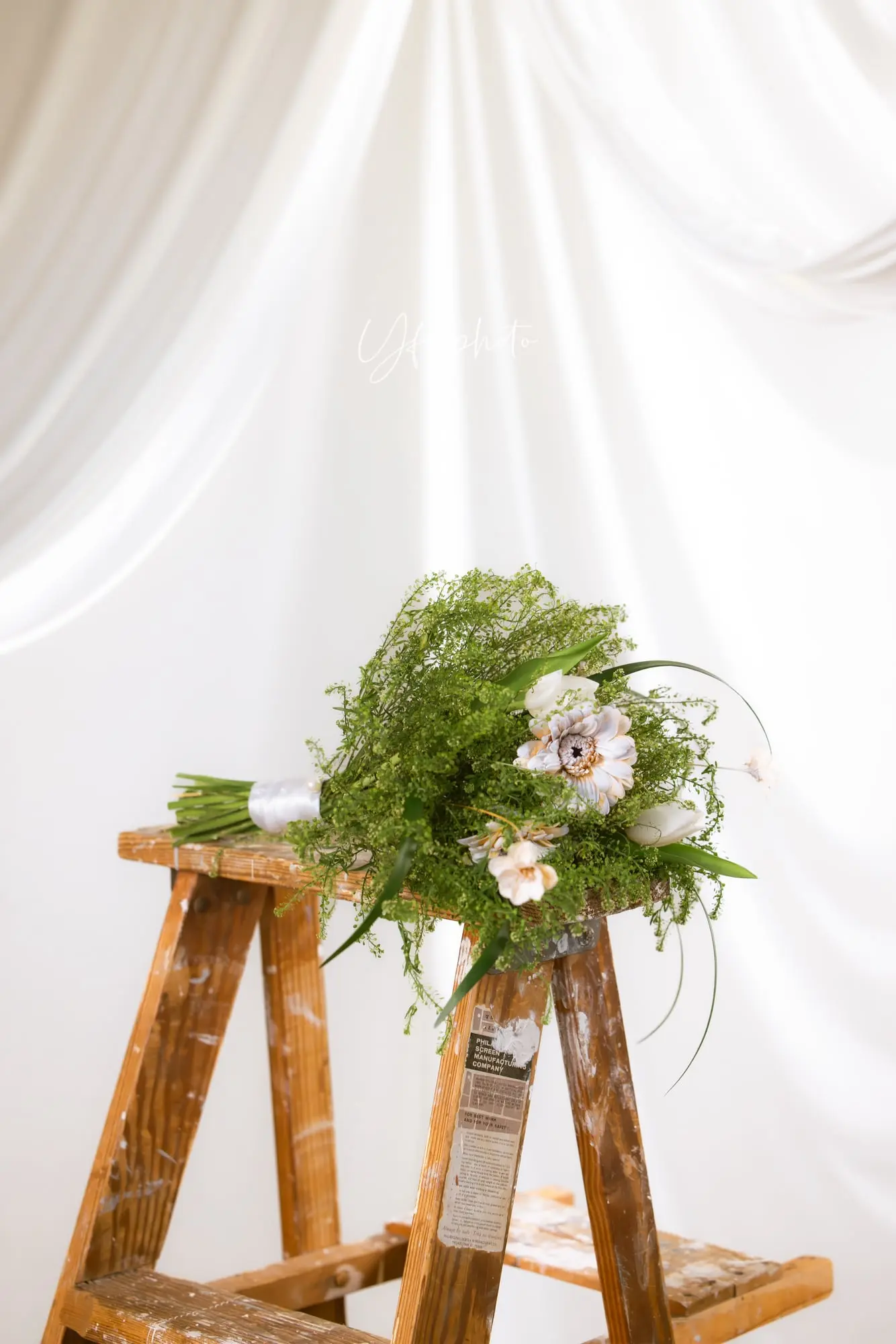 Hand-tied bouquet of airy greens, white tulips and a cream gerbera resting on a vintage wooden ladder