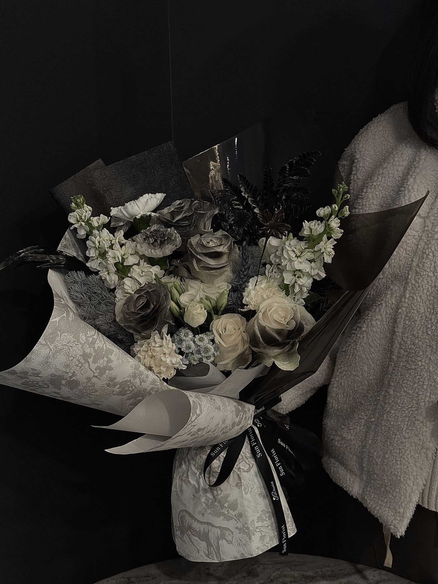 A mesmerizing blend of black, gray, and ivory roses, delicate white florals, and lush foliage , this bouquet evokes the mystery and allure of a misty forest.