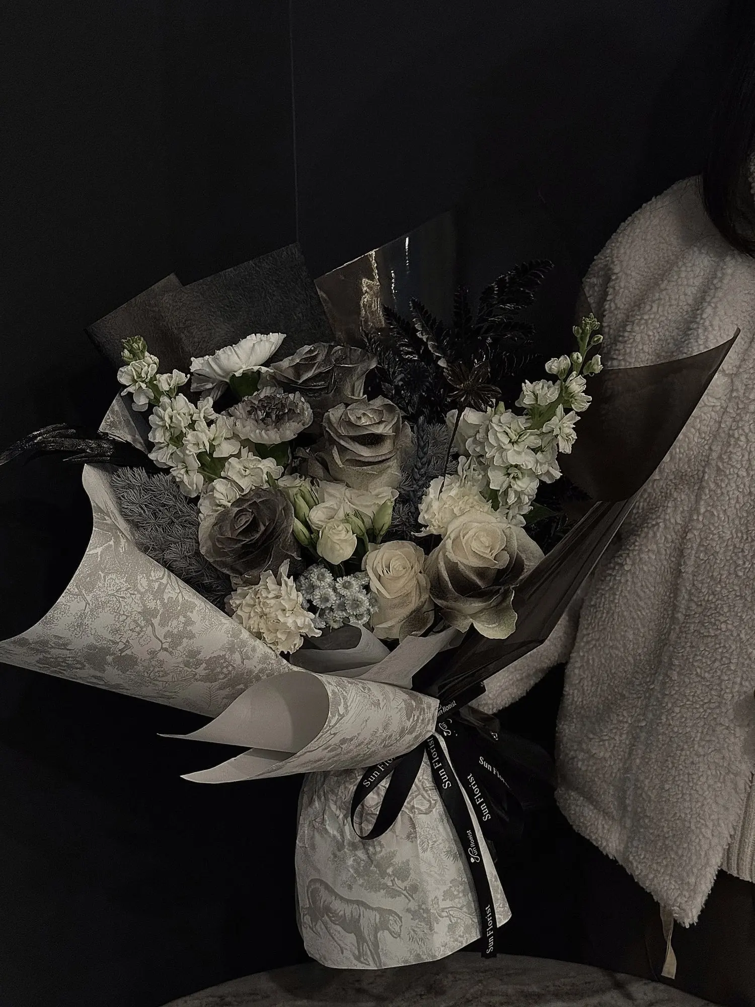 A mesmerizing blend of black, gray, and ivory roses, delicate white florals, and lush foliage , this bouquet evokes the mystery and allure of a misty forest.